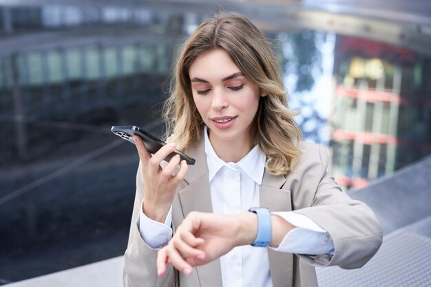 Businesswoman checks time on digital watch and records voice message arranges a meeting sits outside
