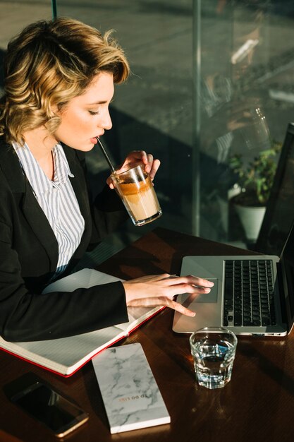 Businesswoman drinking chocolate milkshake while using laptop in restaurant