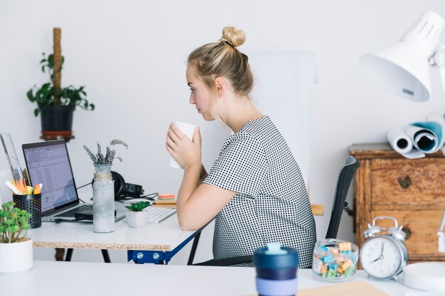 Businesswoman drinking coffee while working in office