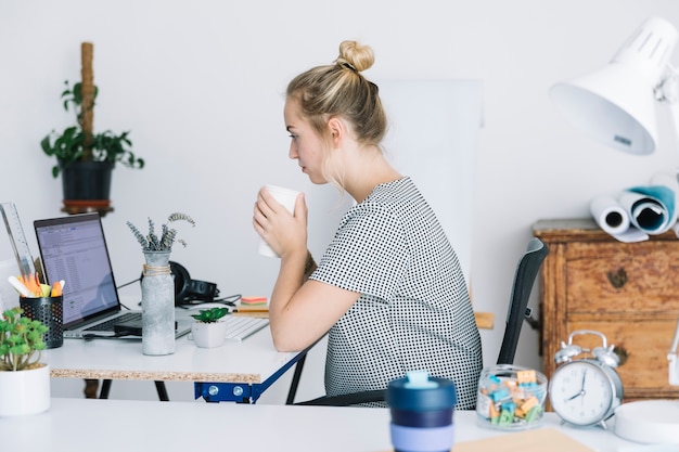 Businesswoman drinking coffee while working in office