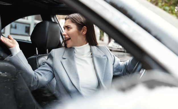 Businesswoman driving car, looking annoyed behind and complaining.