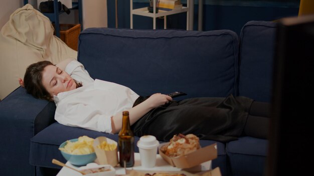 居間のテイクアウトファーストフード店から食事を食べた後、ソファで眠りに落ちる実業家。テーブルの上で食事をしながらテレビを見ながら仕事の後にソファに横になっている眠い人