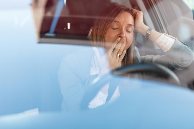 businesswoman feeling tired and yawning while driving a car the view is through the glass