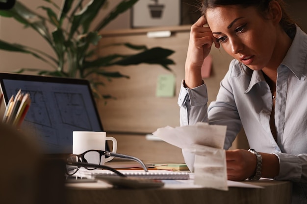 Businesswoman feeling worried about financial debts and analyzing bills while working in the office