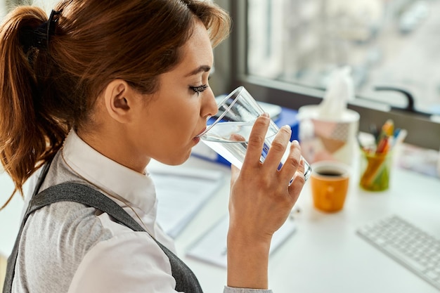 Free photo businesswoman having a glass of water while working un the office