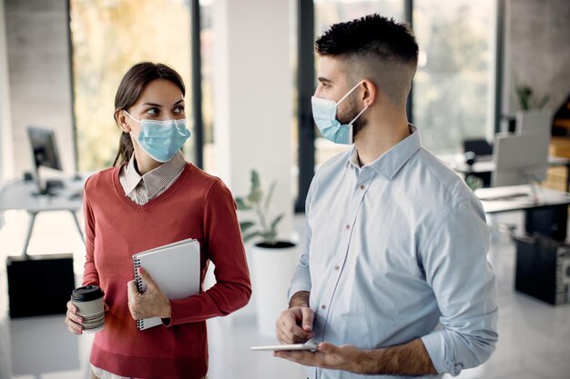 Businesswoman and her colleague wearing face masks while talking in the office