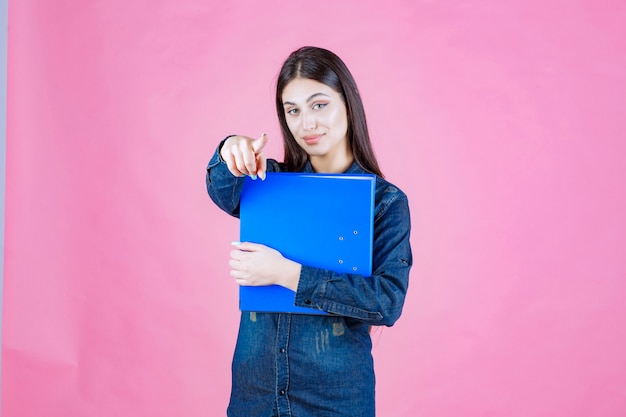 Businesswoman holding a blue folder and pointing you