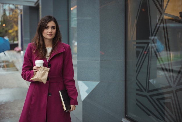 Businesswoman holding disposable coffee cup, parcel and diary