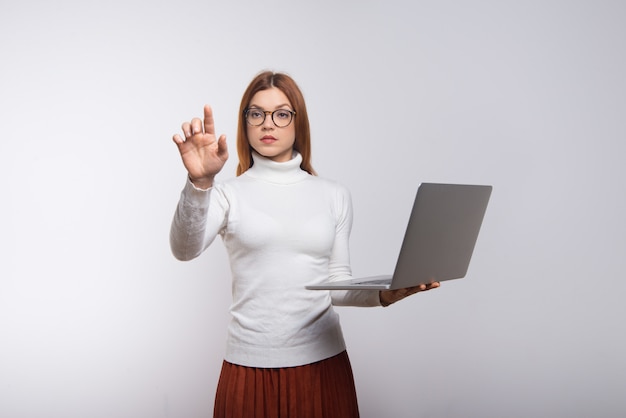 Businesswoman holding laptop and touching air with hand