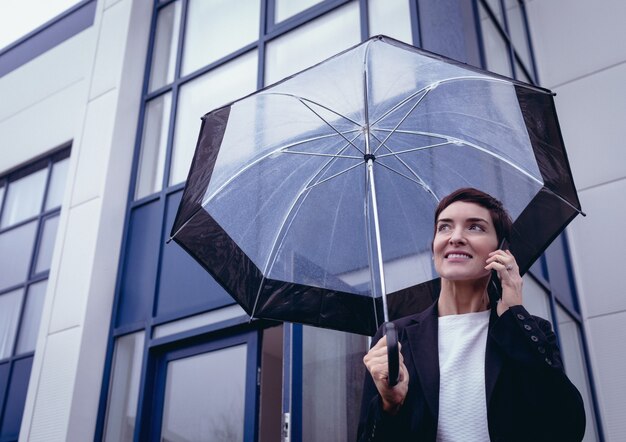 Businesswoman holding umbrella while talking on mobile phone