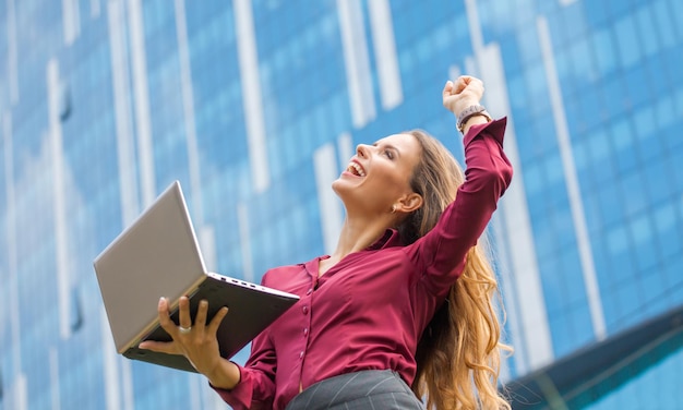 Businesswoman is the winner of agreement between companies in the city Woman with long hair is the professional She is holding laptop and big laughing