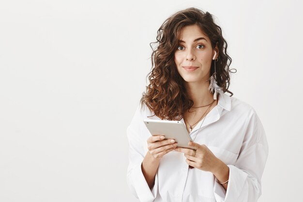 Free photo businesswoman put wireless earbud and hold digital tablet, smiling