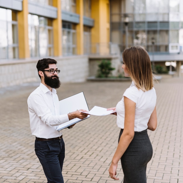 Businesswoman receive document from businessman with city building at background