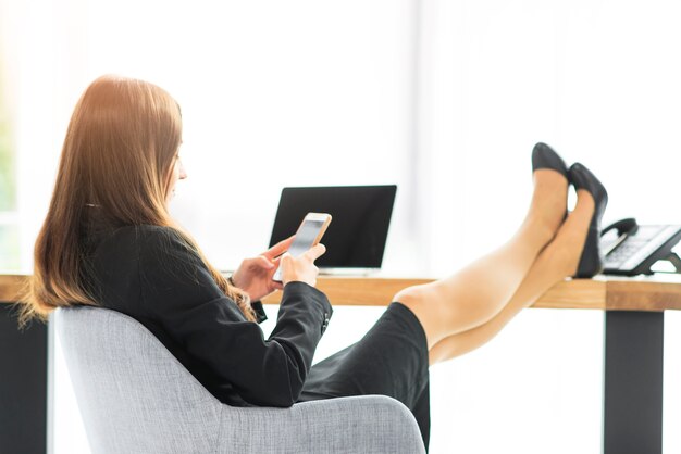 Businesswoman relaxing at desk using smartphone in the office