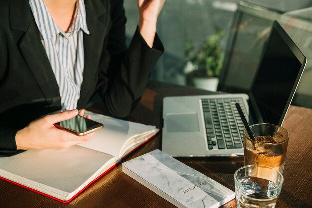 Businesswoman's hand holding cellphone with laptop and chocolate milkshake on wooden desk