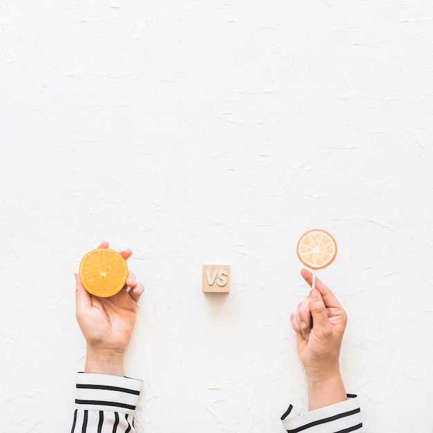 Free photo businesswoman's hand holding citrus slice versus lollipop over white background