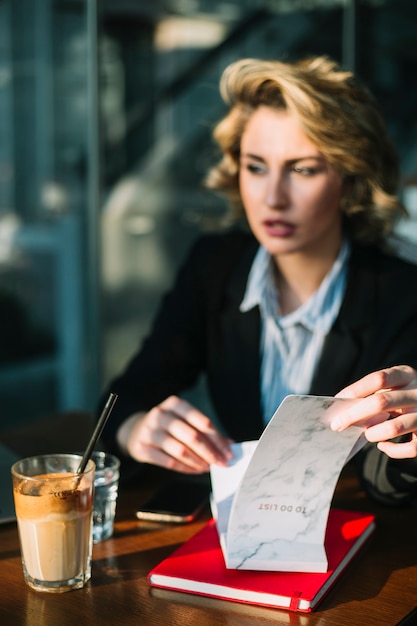 Free photo businesswoman's hand holding to do list with chocolate milkshake on wooden desk