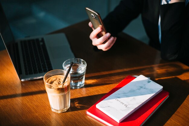 携帯電話をラップトップで使用しているビジネスマンの手;チョコレートミルクセーキと木製の机の本