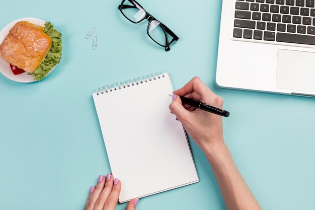 Businesswoman's hand writing on the spiral notepad with pen over the office desk