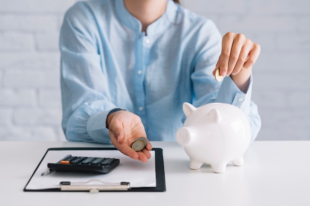 businesswoman showing coins with white piggybank on desk