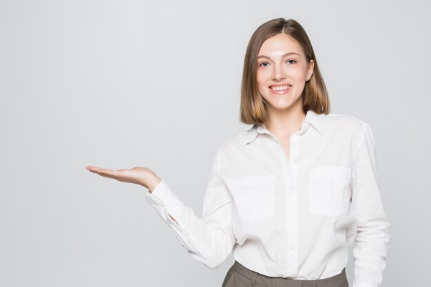 Businesswoman showing copy space for product with open hand palm. Smiling friendly expression on young businesswoman wearing glasses isolated on white wall.