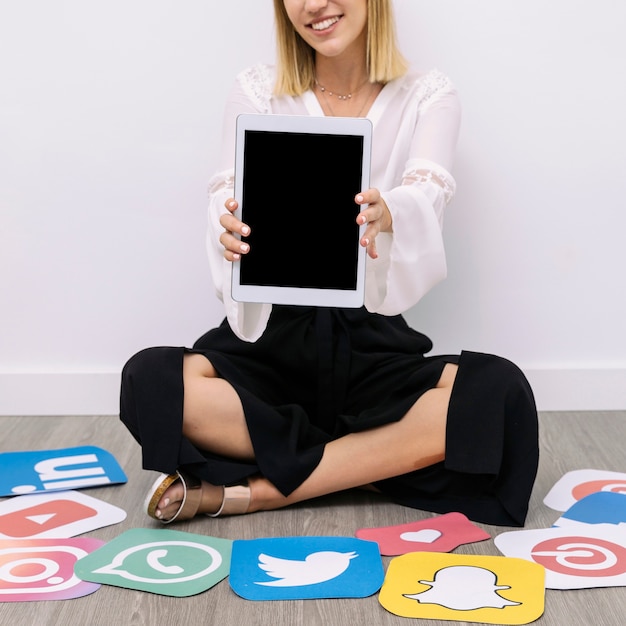 Businesswoman sitting on floor with social media icons showing digital tablet