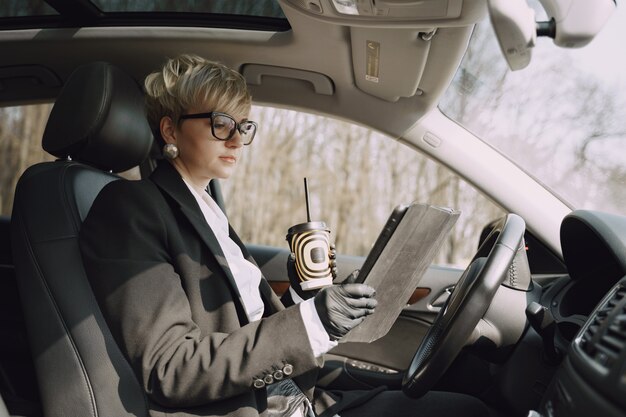 Businesswoman sitting inside a car and drinks a coffee