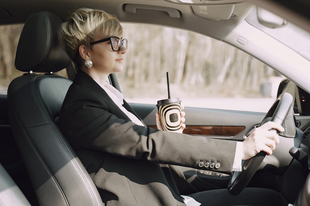 Businesswoman sitting inside a car and drinks a coffee