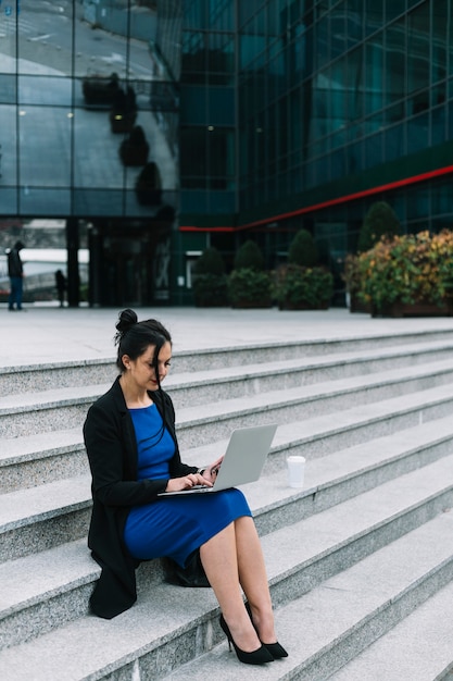 Businesswoman sitting on staircase working on laptop