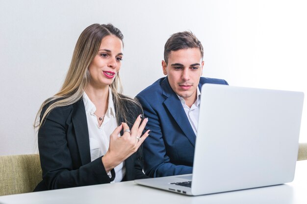Businesswoman sitting with businessman looking at laptop gesturing