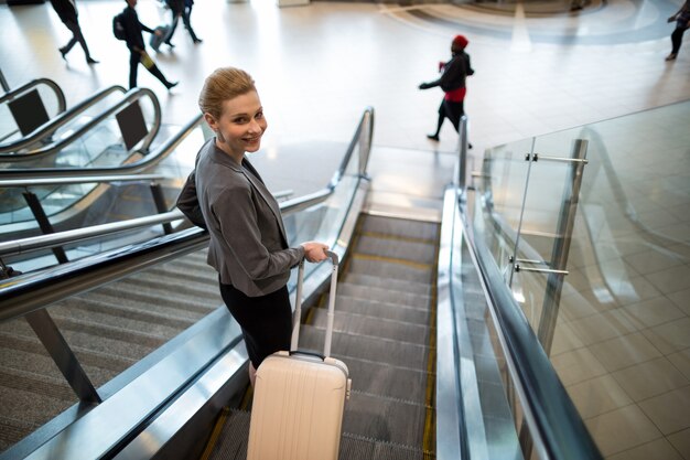 Businesswoman standing on escalator with luggage