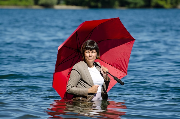 Free Photo businesswoman in a suit standing in the water and holding a red umbrella