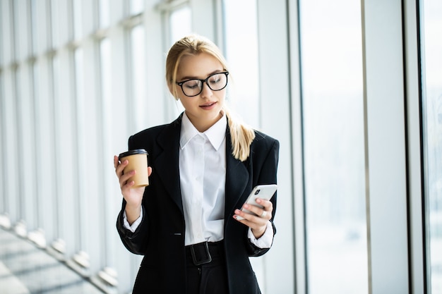 Коммерсантка принимая перерыв на чашку кофе и используя smartphone в офисе
