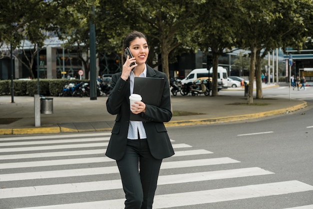 Foto gratuita donna di affari che parla sul telefono cellulare che attraversa la strada