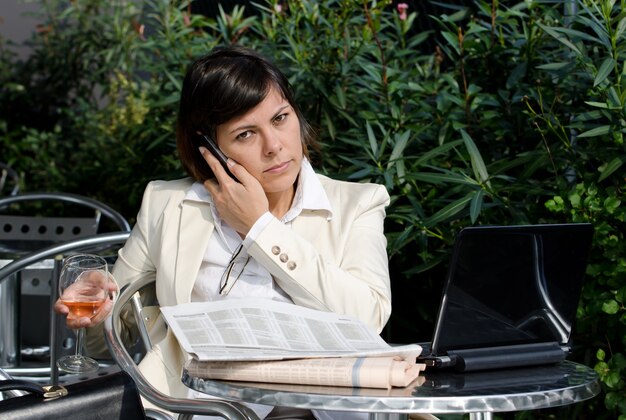 Businesswoman talking on the phone while working with documents and holding a glass of wine