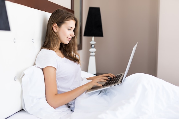 La donna di affari usa il suo laptop nel letto la mattina presto