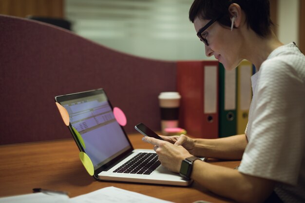 Businesswoman using mobile phone while working on laptop