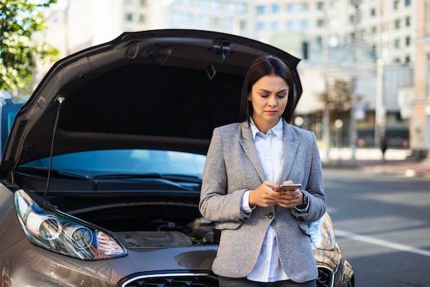 彼女の壊れた車の助けを得るためにスマートフォンを使用して実業家