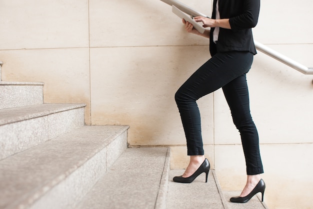 Businesswoman walking upstairs and using touchpad