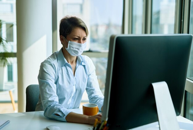 オフィスでデスクトップPCで作業中にフェイスマスクを身に着けている実業家