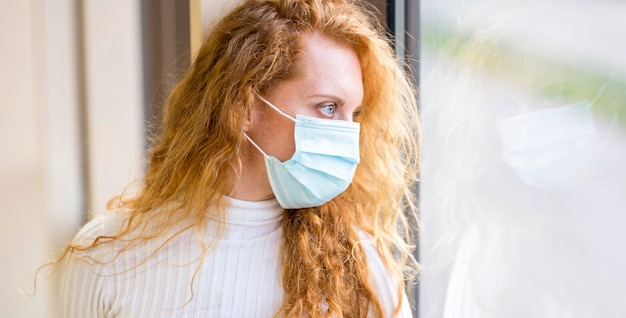 Foto gratuita imprenditrice che indossa una maschera e guardando fuori dalla finestra