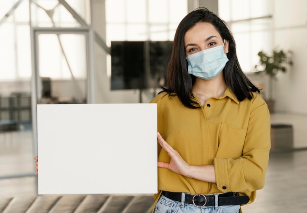 Free photo businesswoman wearing a medical mask at work while holding a blank card