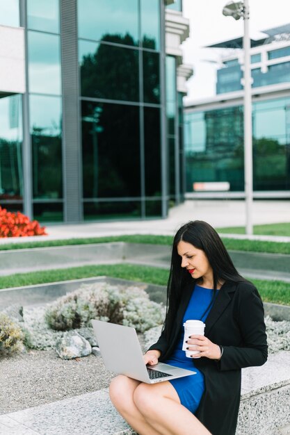 Businesswoman with disposal cup using laptop at outdoors