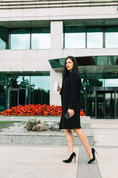 Free photo businesswoman with disposal cup walking in front of building