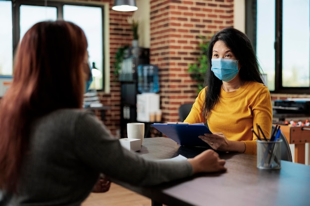 Businesswoman with face mask interviewing potential manager discussing business collaboration during interview meeting in startup office. Team working at management startegy during coronavirus