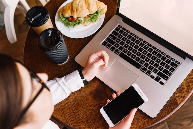 Бесплатное фото Бизнес-леди с ноутбуком и смартфоном в кафе