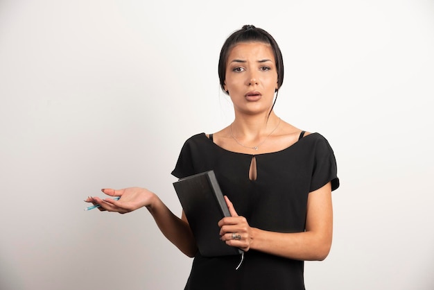 Businesswoman with notebook standing on white wall.