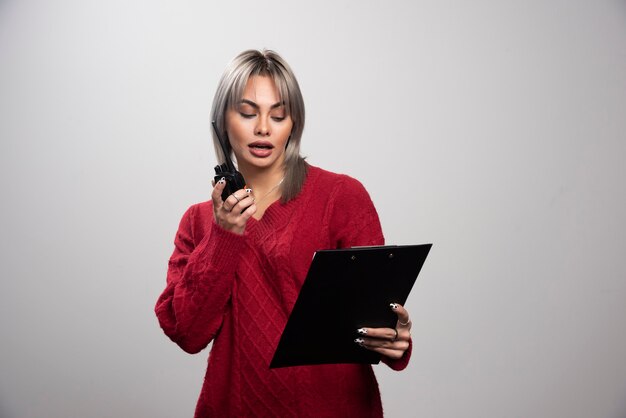 Businesswoman with radio transceiver looking at clipboard.