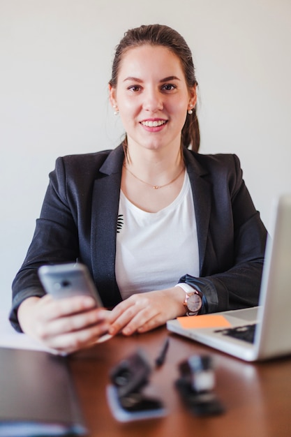 Businesswoman with smartphone at laptop