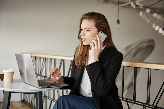 Free photo businesswoman working in cafe, answer calls and looking at laptop